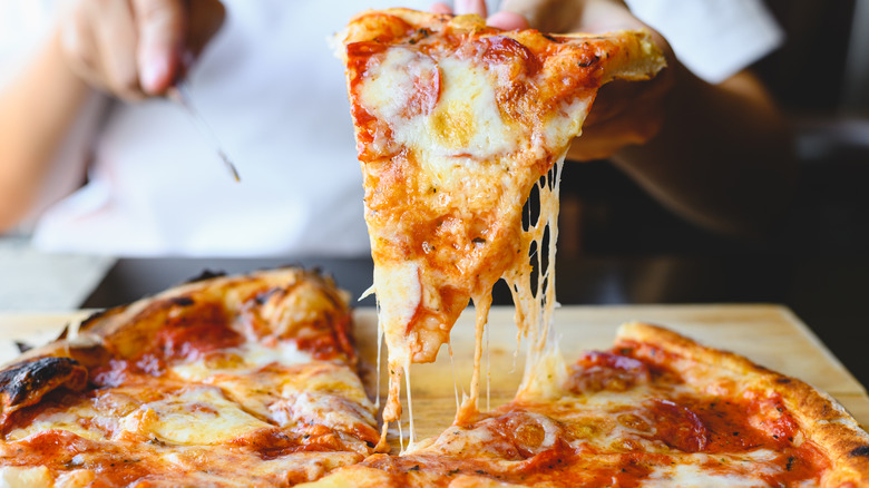 Hand lifting cheesy pizza slice