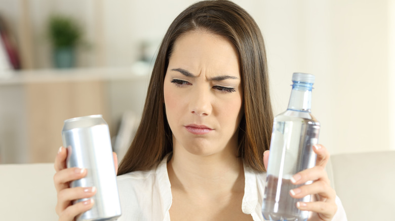 Woman holding bottle and can with perplexed expression