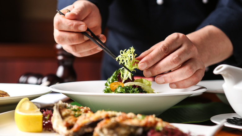 Restaurant chef plating a dish with salad greens