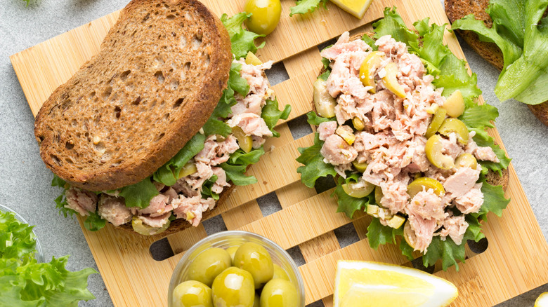 Overhead view of tuna salad sandwich with small bowl of olives and a nearby lemon wedge.