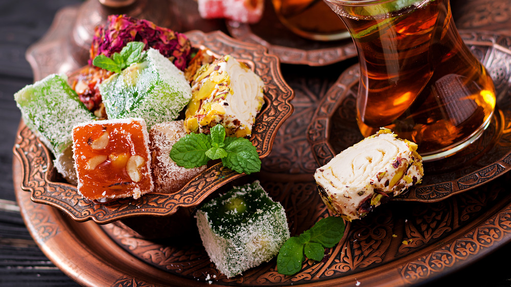 Bowl with various pieces of turkish delight lokum and black tea with mint on a dark background