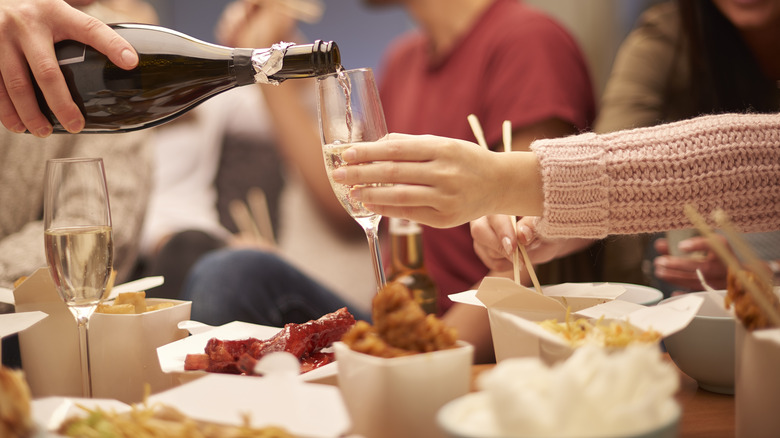 pouring wine into a glass and eating Chinese takeout