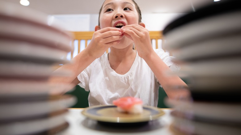 Girl eating sush at restaurant with stack of plates out of focus