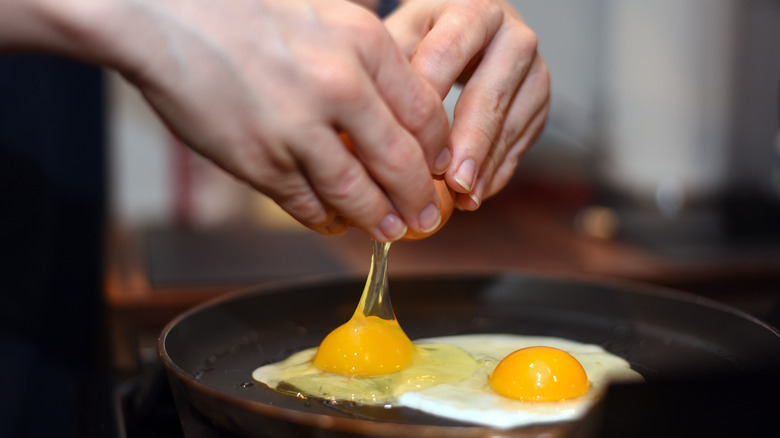 person cracking eggs in pan