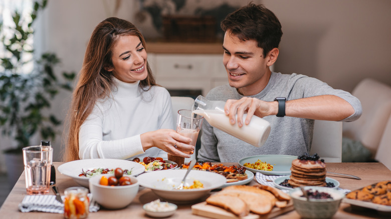 Man pouring plant-based milk for smiling woman