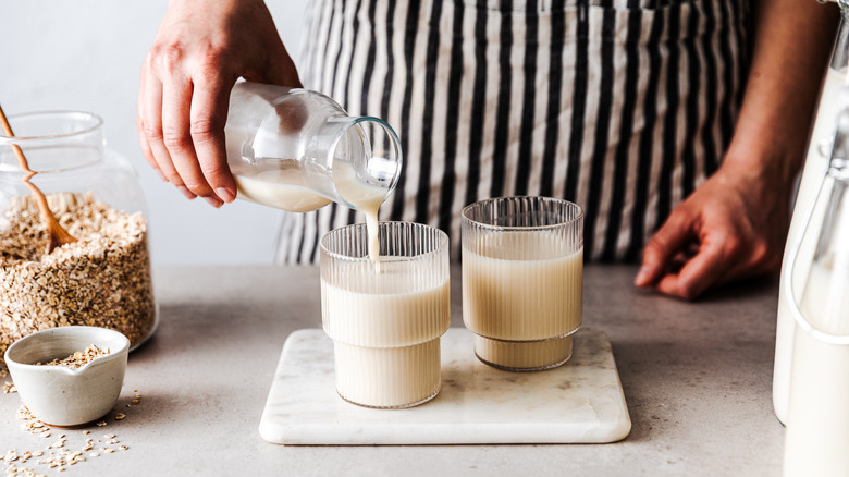 Hands pouring glasses of oat milk