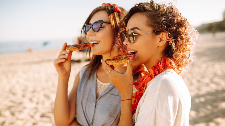 women eating pizza on the beach