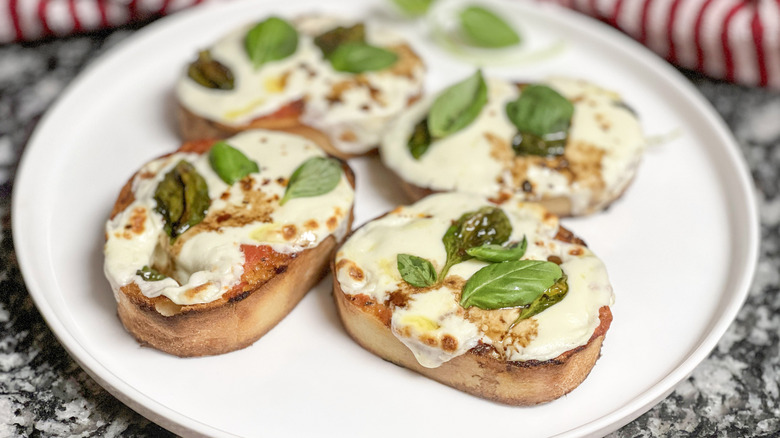 Toasted bread with melted cheese and basil leaves on a white plate