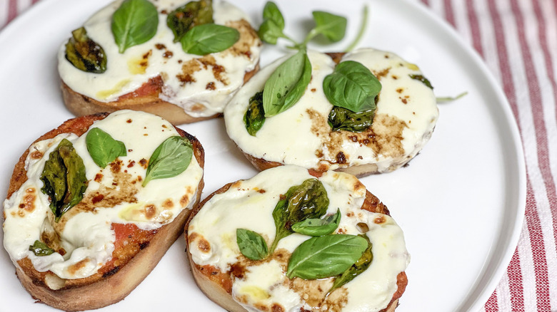 Toasted bread with melted cheese and basil leaves on a white plate