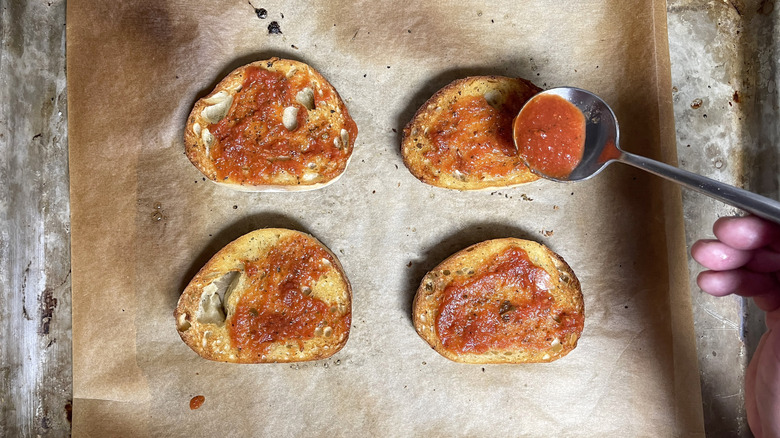 Hand spooning tomato sauce on toast