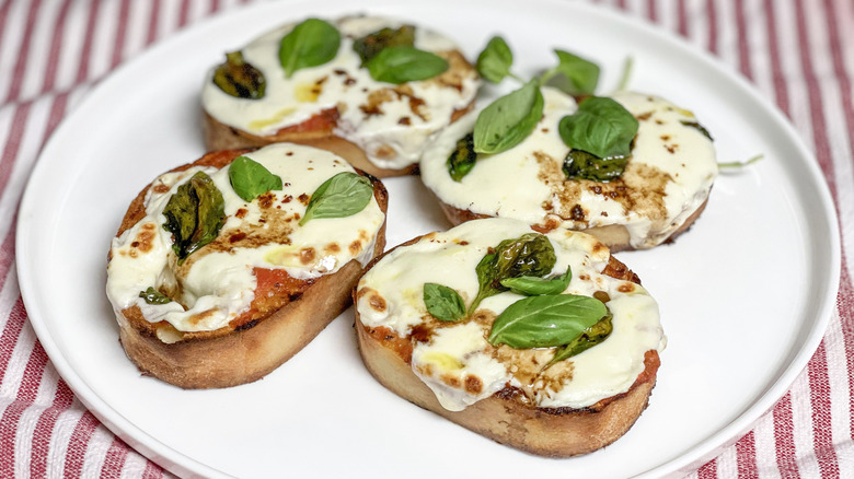 Toasted bread with melted cheese and basil leaves on a white plate