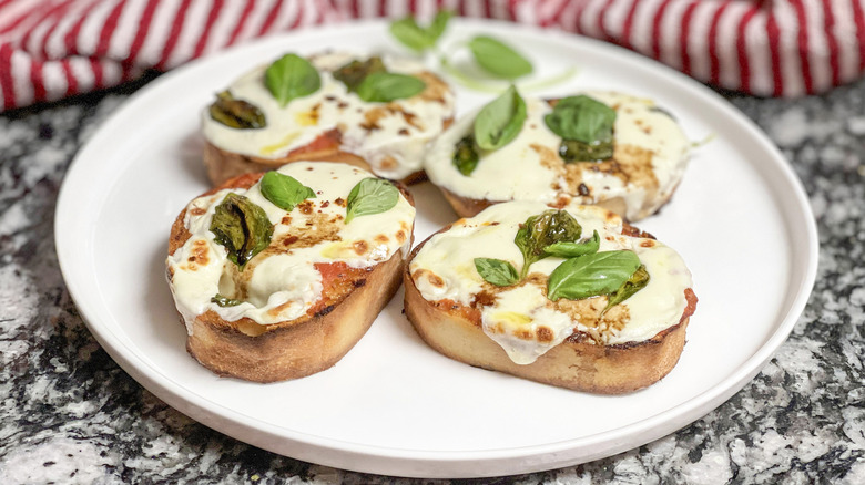 Toasted bread with melted cheese and basil leaves on a white plate