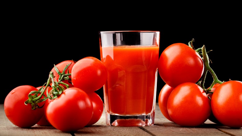 A glass of tomato juice with some tomatoes 