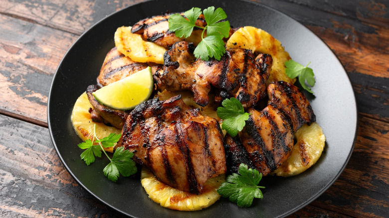 Huli huli chicken with pineapple, cilantro, and lime on a black plate