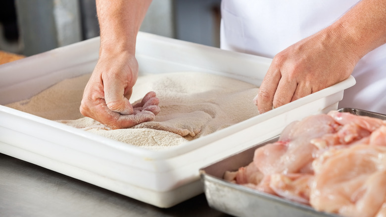 hands dredging chicken in flour