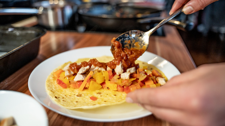 person spooning salsa on taco