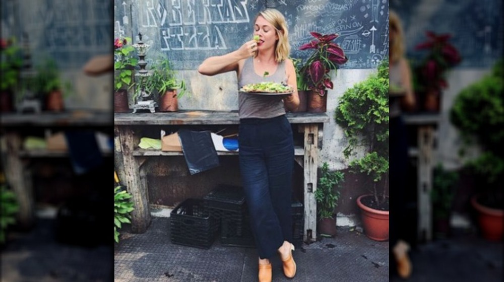 Alison Roman eating from a plate while standing