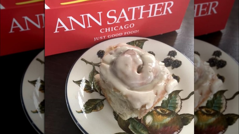 Cinnamon roll on a plate next to Ann Sather box