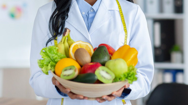 Smiling dietitian holding out a bowl of fruits and vegetables