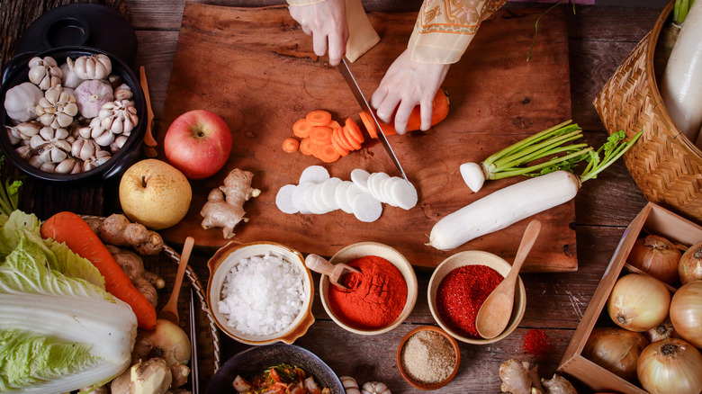 Hands chopping a carrot on a table with other foods