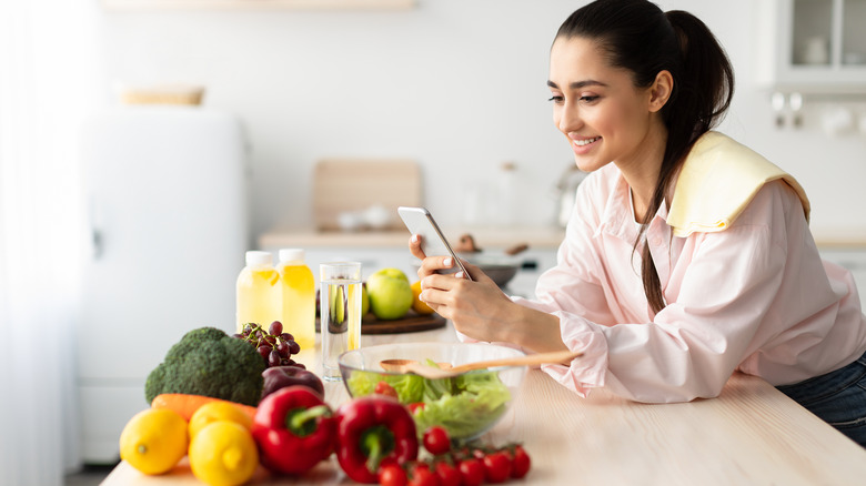 Smiling woman looking at cellphone with fruits and vegetables nearby