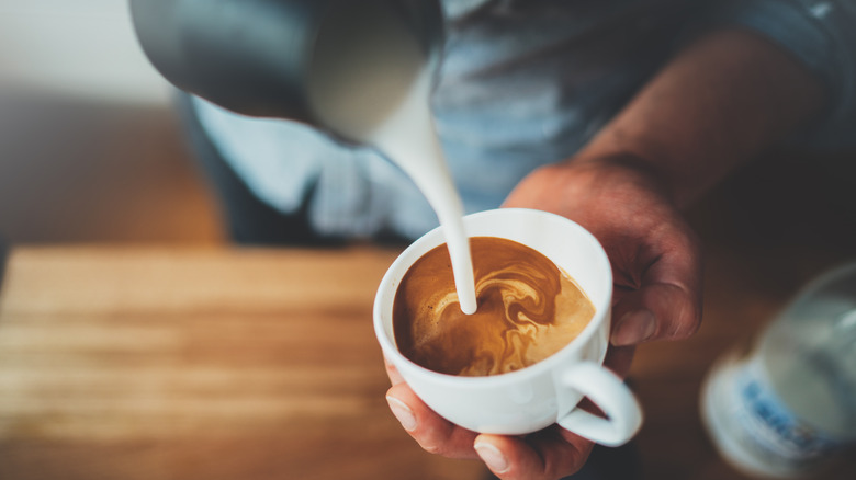 Barista pouring milk over espresso in a mug