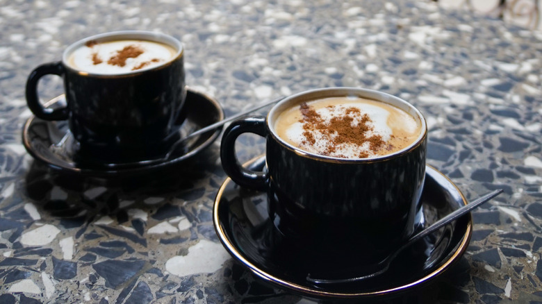 Two full coffee mugs on saucers with spoons