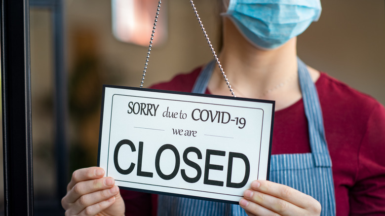 Masked worker turning "closed" sign