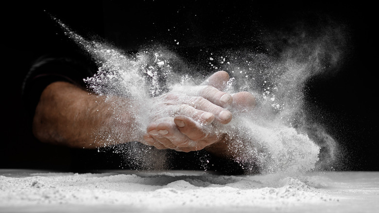 Two hands holding dough among flour