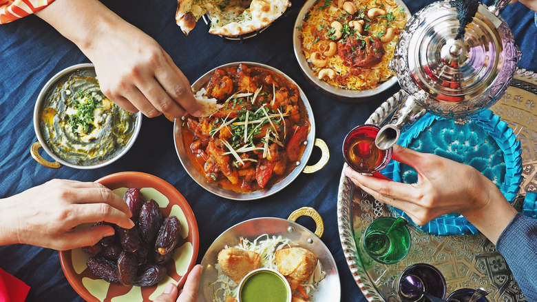 Hands reaching for various foods and pouring tea