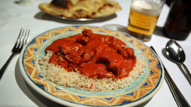 A plate of chicken tikka masala and glass of beer