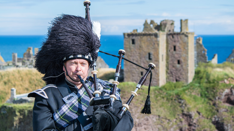 Man in traditional Scottish attire plays bagpipes in castle ruins