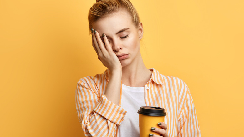 sleepy woman holds cup of coffee