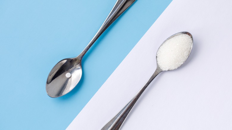 Two teaspoons, one with a white sugar-like substance, the other with a pill