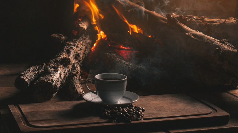 Cup of coffee and coffee beans by wood fire