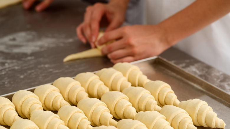 hands rolling croissants on tray