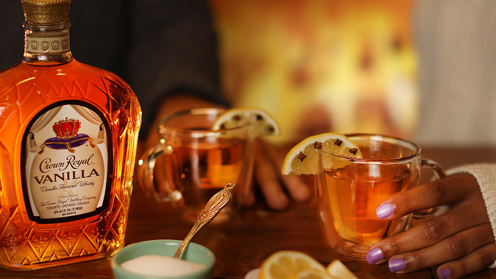 Crown royal bottle with hot toddy ingredients and hands holding glasses