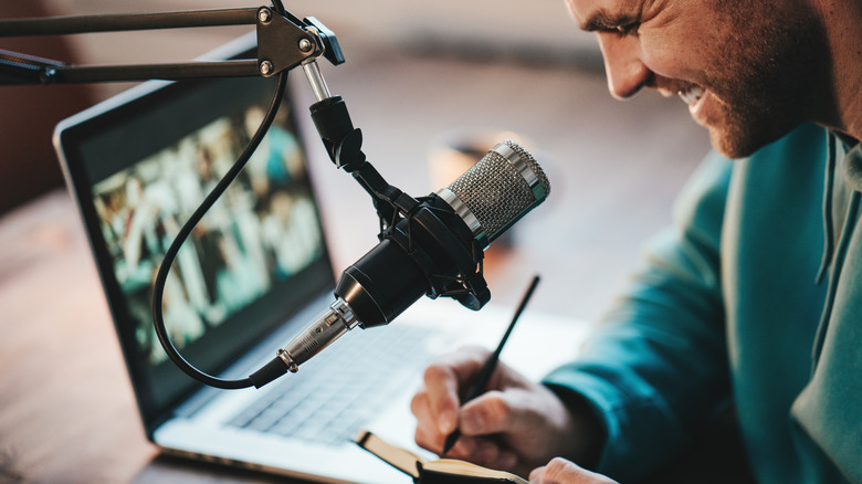 Podcaster with microphone writing in notebook