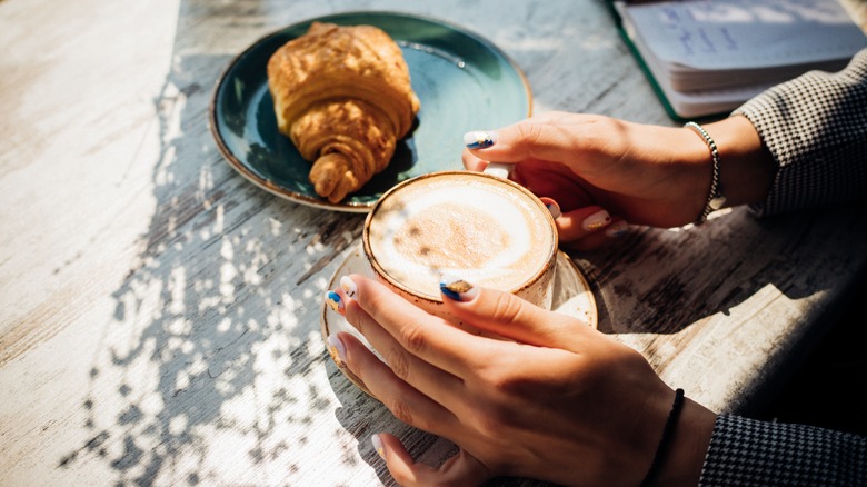 hands holding cappuccino with croissant