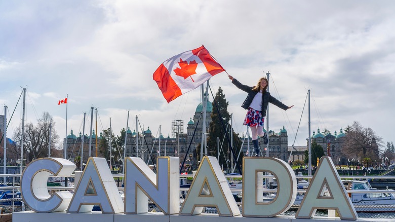 Woman waving Canadian flag standing on large Canada letters.