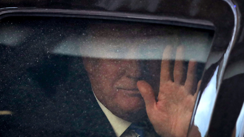 Donald Trump as President waving from behind a glass window of a limo