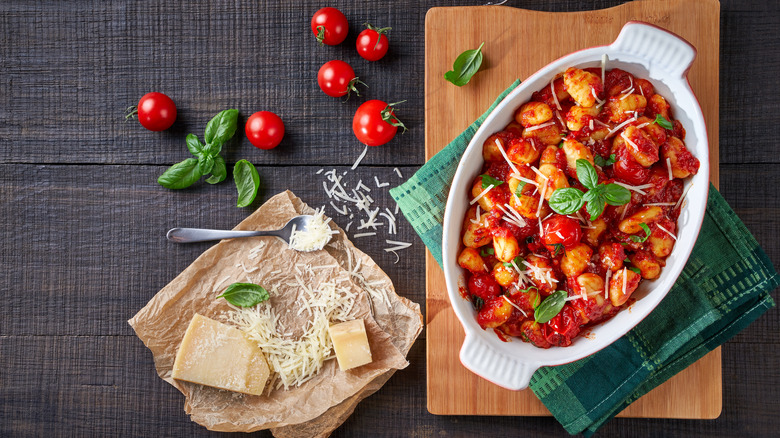 baked gnocchi in a dish next to parmesan cheese and tomatoes