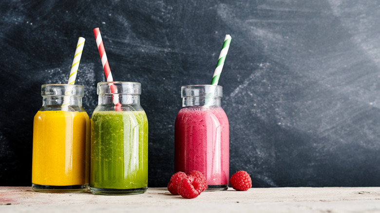 Mango, vegetable and raspberry fruit juice smoothies with candy cane color straws on wooden table in front of chalkboard background