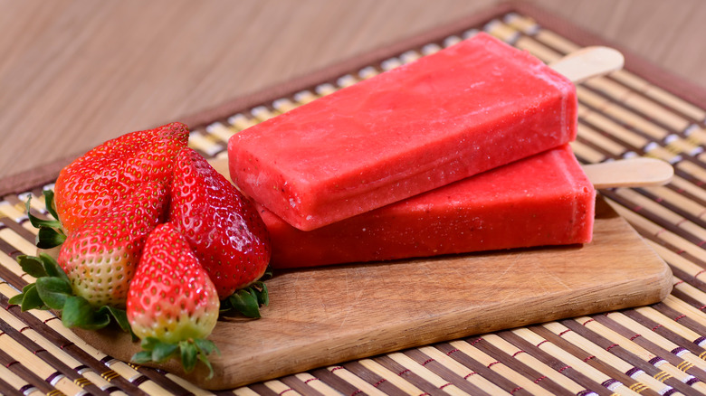 Two strawberry paletas and strawberries on table