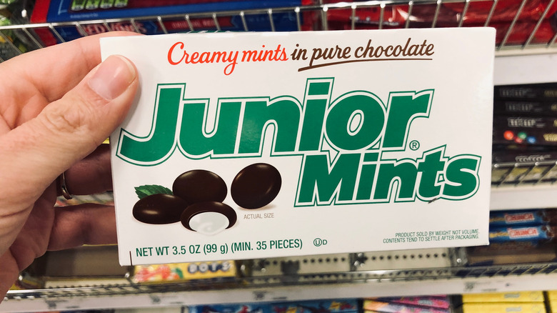 Hand holding box of Junior Mints in front of candy rack