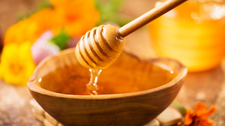 Honey dripping from a wooden dripper into a wooden bowl