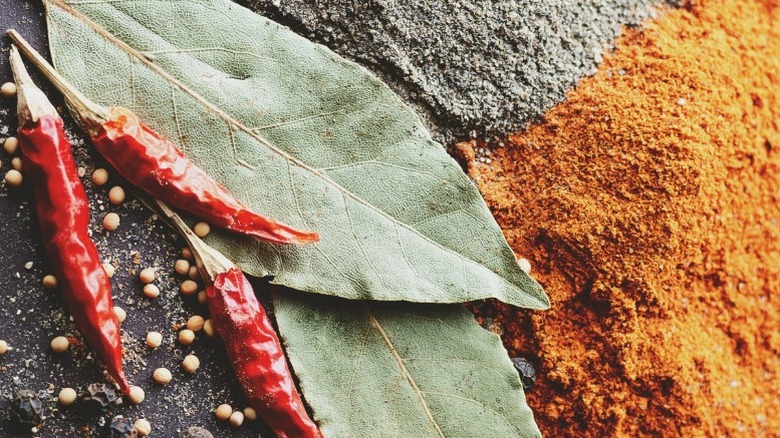 close up of bay leaves, chili peppers, and whole and ground spices on black background