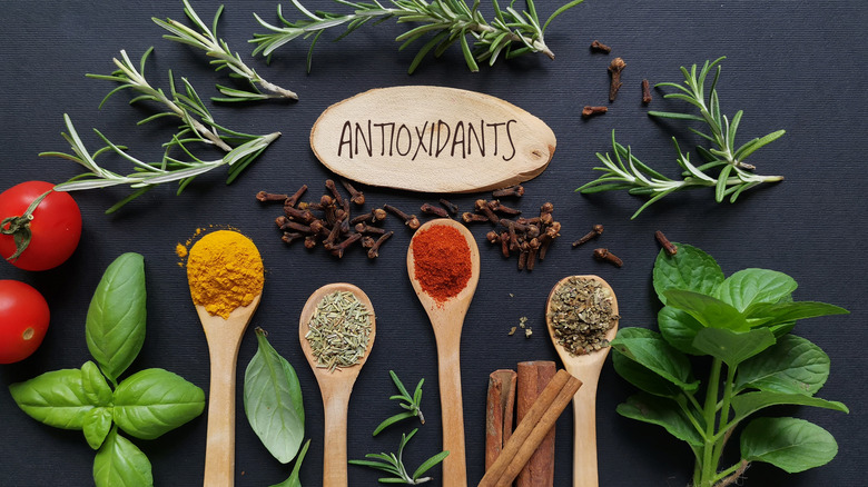 Spices and herbs on black background with wooden sign that says 'antioxidants'