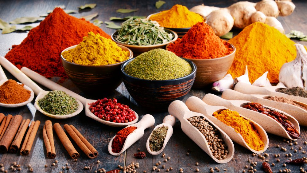 Piles, bowls, and spoons full of brightly colored whole and ground spices 