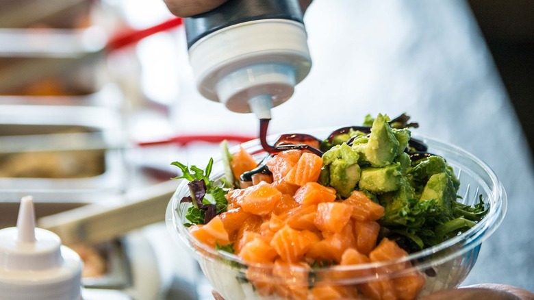 pouring sauce on Poke Bros. bowl